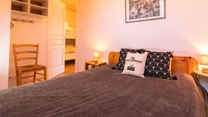 Una camera da letto con un letto, una sedia, un comodino con una lampada, uno scaffale con un quadro e un'immagine appesa al muro.