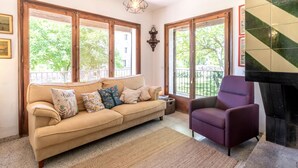 A living room with a beige sofa, a purple armchair, a fireplace, and large windows with a view of greenery.