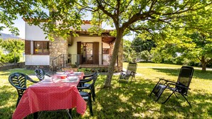 A patio with a table set for dining, surrounded by chairs, and a tree providing shade.