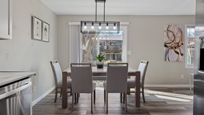A modern kitchen with a dining area, featuring a large window, a chandelier, and a painting on the wall. - Modern 5BR Sleeps 12 Fire Pit 85" TV Decatur (Decatur)