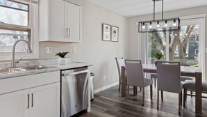 A modern kitchen with white cabinets, stainless steel appliances, and a dining area with wooden chairs and a table. - Modern 5BR Sleeps 12 Fire Pit 85" TV Decatur (Decatur)