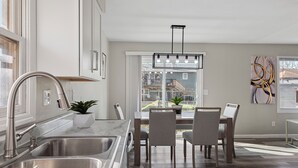 A modern kitchen with a large window, stainless steel sink, and a dining area with a table and chairs. - Modern 5BR Sleeps 12 Fire Pit 85" TV Decatur (Decatur)