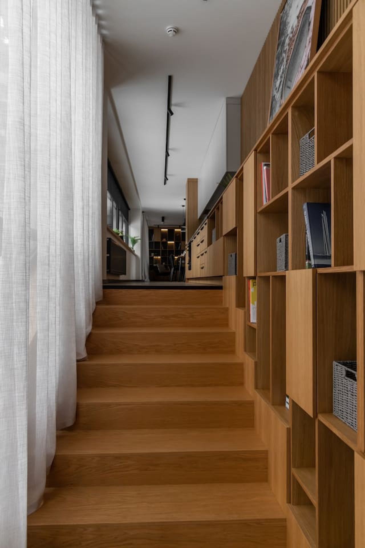 Eine Treppe führt zu einem Raum mit einem Holzbücherregal und Blick auf einen Küchenbereich.