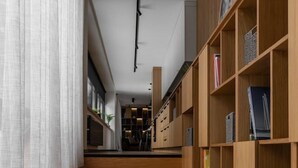 Un escalier menant à une pièce où se trouve une bibliothèque en bois et d’où l’on a vue sur un espace cuisine.