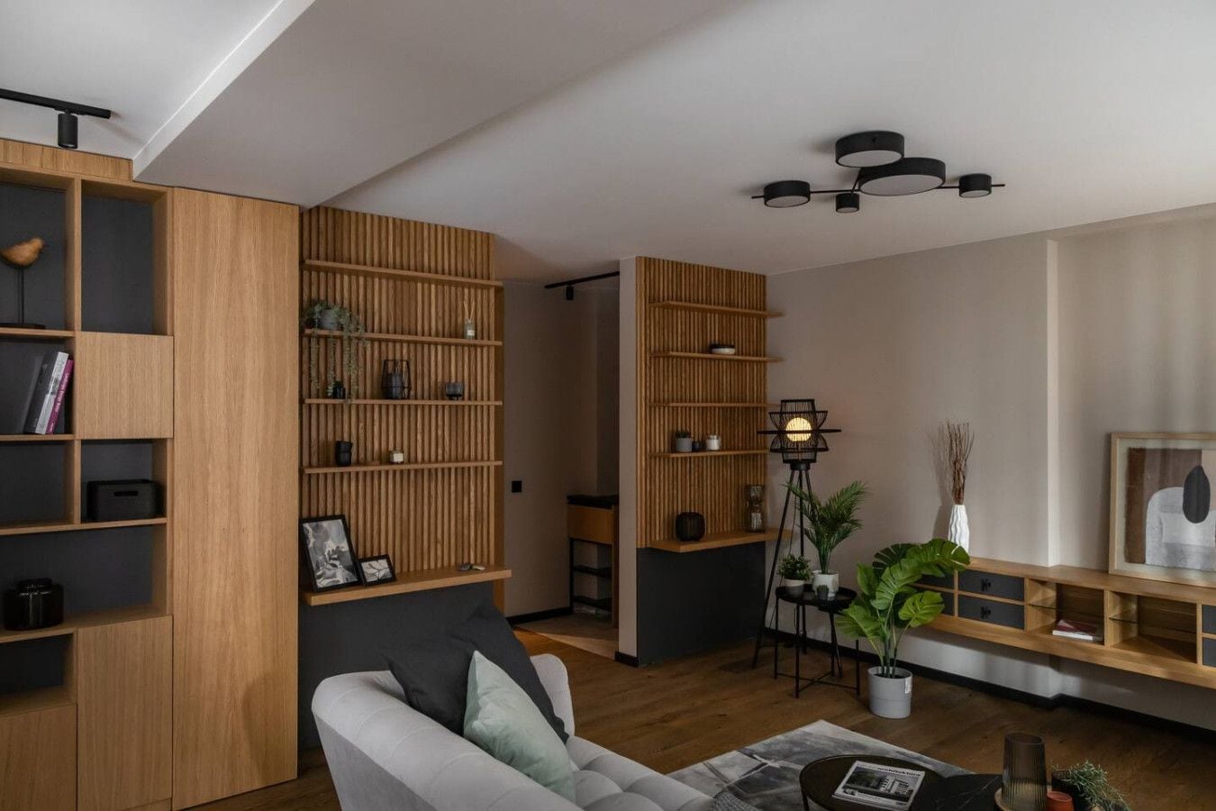 Un salon moderne avec des étagères en bois, un lampadaire noir et un canapé gris.