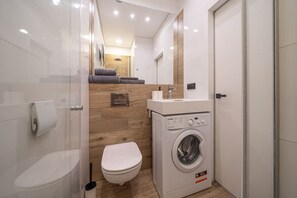 Een kleine badkamer met toilet, wasmachine en een klein wastafeltje.