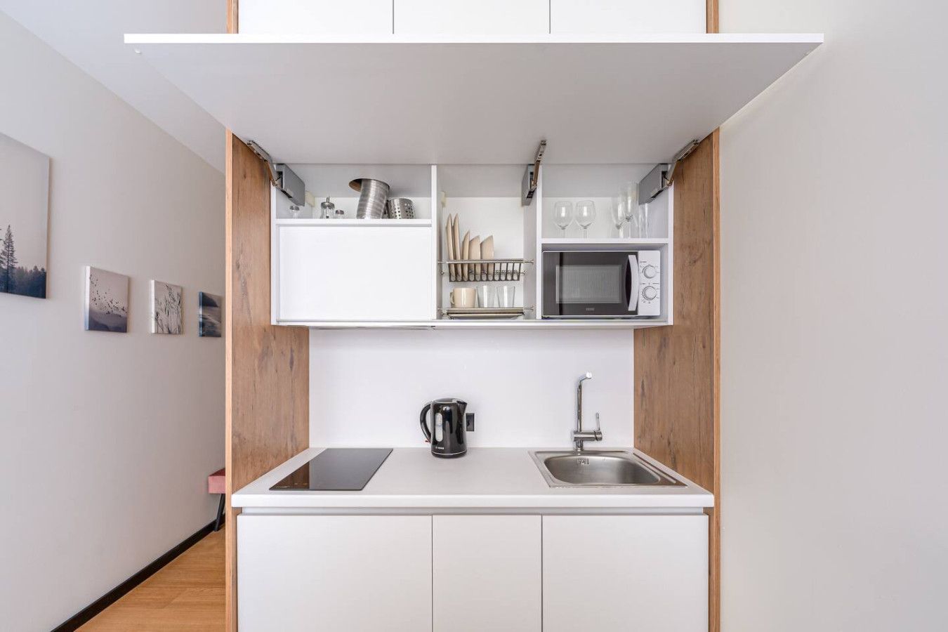 A compact kitchen with white cabinets, a microwave, a kettle, and a sink.