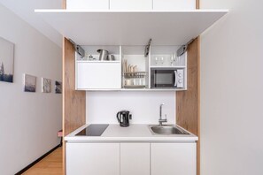 A compact kitchen with white cabinets, a microwave, a kettle, and a sink. - Dzintari Light-Filled Studio next to Sea & Park (Jurmala)