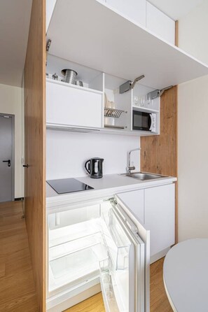 Een compacte keuken met witte kastjes, een magnetron, een waterkoker en een spoelbak.