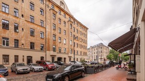 En gade med parkerede biler og en bygning med mange vinduer og altaner.