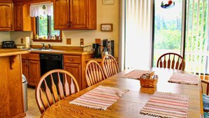 Une cuisine avec des meubles en bois, une table à manger avec des sets de table, et une vue sur la verdure par la fenêtre.
