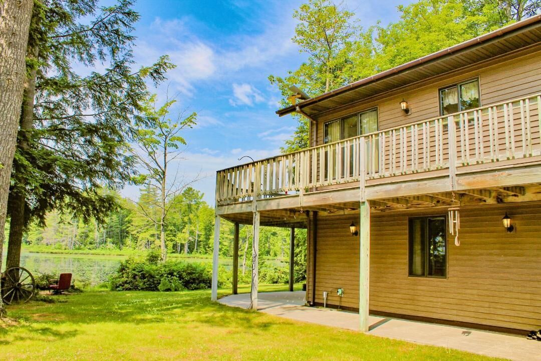 Eine zweistöckige Holzhütte mit Balkon, umgeben von üppigem Grün und einem See.