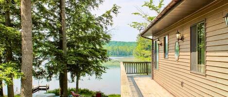 A wooden cabin with a deck overlooking a lake, surrounded by trees.