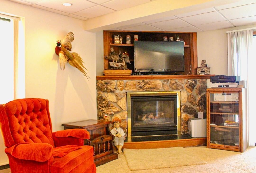 A living room with a fireplace, a television mounted above it, a red armchair, and a small statue.