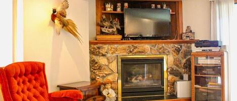 A living room with a fireplace, a television mounted above it, a red armchair, and a small statue.