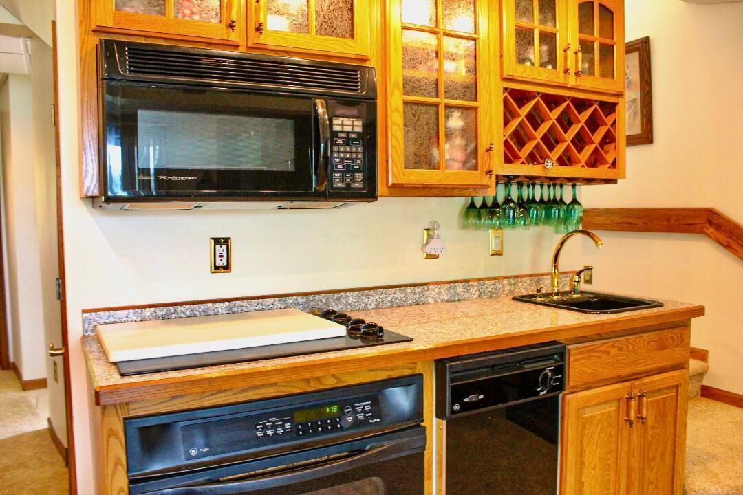 Una cocina con armarios de madera, microondas, lavavajillas y una estantería para vinos.