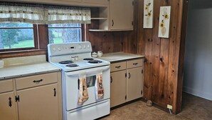 A kitchen with wooden cabinets, a white stove, and a window with curtains.