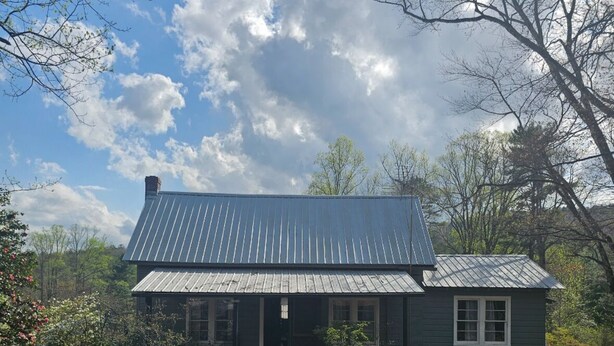 A two-story house with a metal roof, surrounded by trees and a grassy yard.