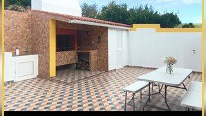 An outdoor patio with a stone wall, a tiled floor, a white table, and a flower vase. - Herdade das Hortênsias (São Jorge)