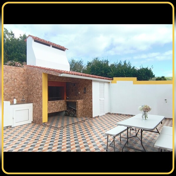 An outdoor patio with a stone wall, a tiled floor, a white table, and a flower vase. - Herdade das Hortênsias (São Jorge)