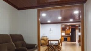 A spacious living room with a sofa, a wooden dining table, and a kitchen area in the background. - Herdade das Hortênsias (São Jorge)