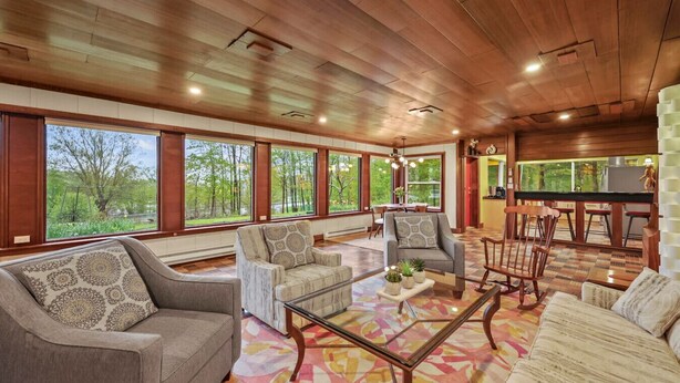 A spacious living area with large windows, a wooden ceiling, and a cozy seating arrangement. - Friendly Hills | Passive Home • EV Charger (Pittsfield)