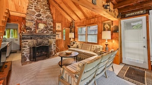 A cozy cabin interior with a stone fireplace, wooden walls, a sofa, and a dining area. - Stockbridge Landings | 3 Mins To Tanglewood (Stockbridge)