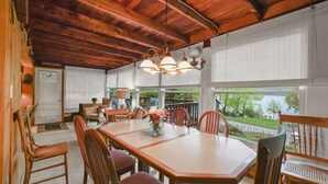 A dining area with a wooden table and chairs, a vase of flowers, and a view of a lake through large windows. - Stockbridge Landings | 3 Mins To Tanglewood (Stockbridge)