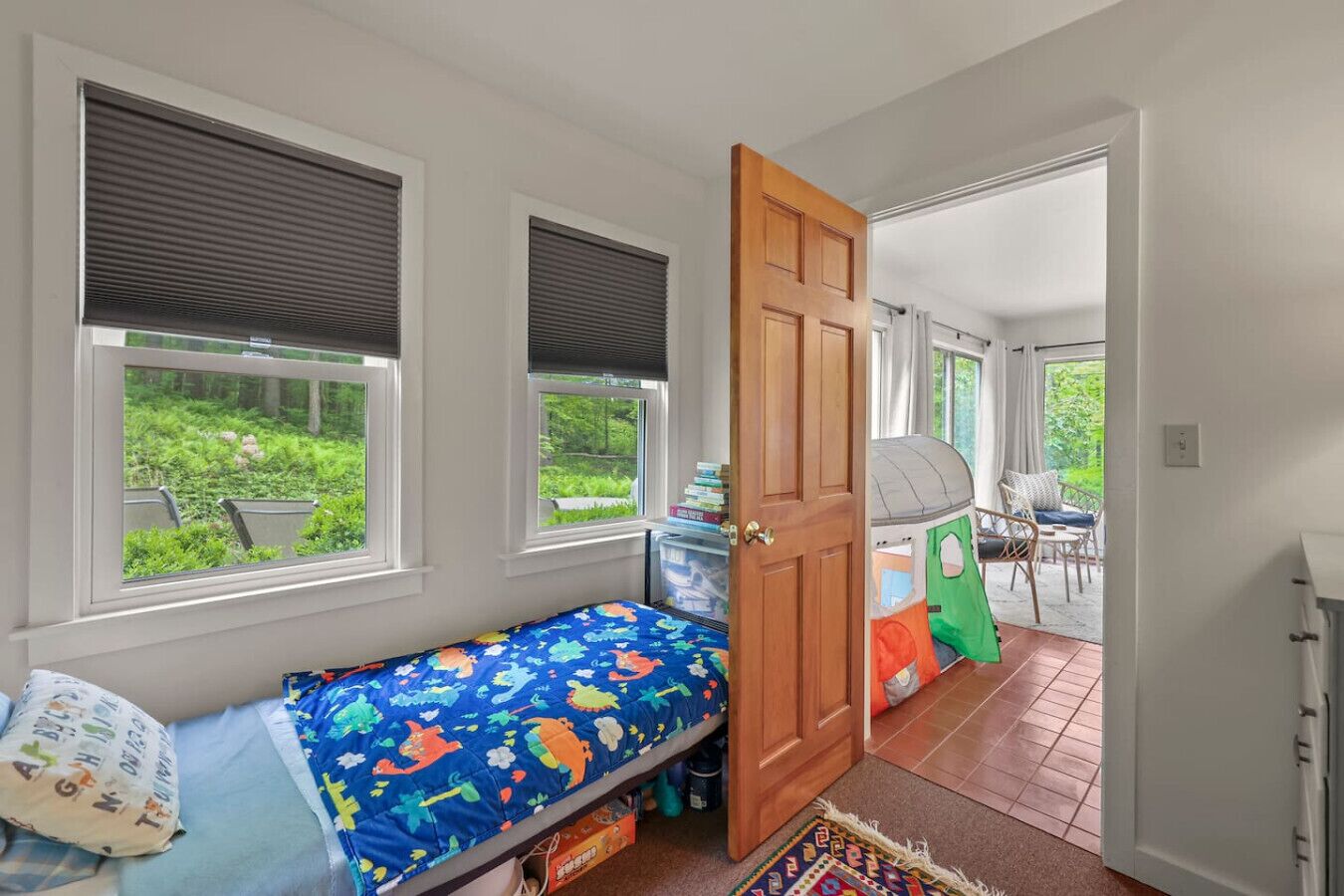 Habitación infantil con cama, dos ventanas, una puerta y vistas a un jardín.