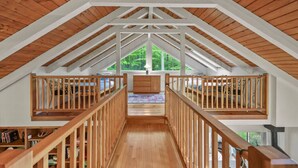 Ein geräumiges Schlafzimmer im Dachgeschoss mit einer Holztreppe, großen Fenstern und Blick ins Grüne.