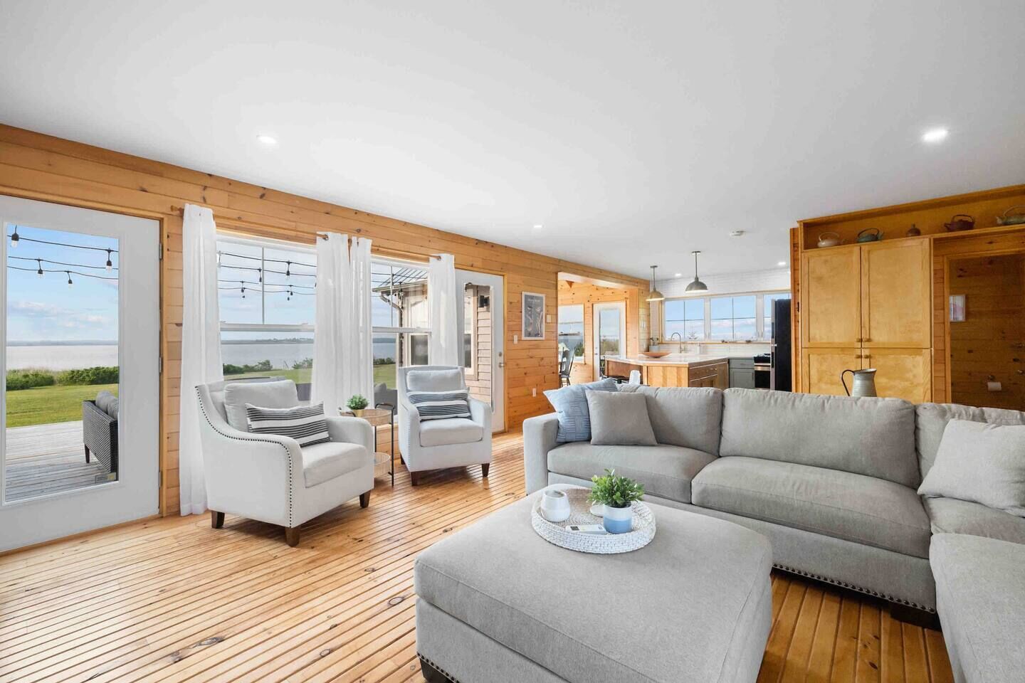 A spacious living area with a large grey sofa, two armchairs, and a wooden floor.