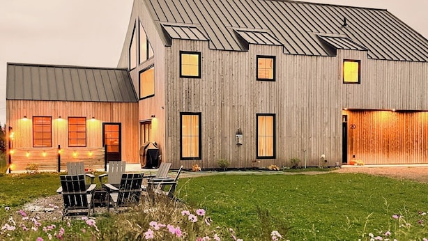 A modern wooden house with a sloped roof, multiple windows, and a well-maintained lawn with flowers.