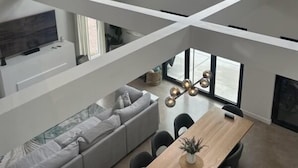 A modern loft with a high ceiling, large windows, a dining area, and a cozy seating area.