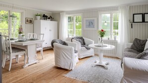 A spacious room with a dining area, a white sofa, and a round table with a vase of flowers. - Vacation home Bygget by Interhome (Simlångsdalen)