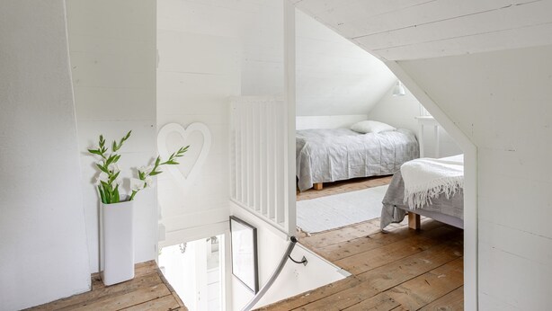 A bedroom with a sloped ceiling, a bed with a grey bedspread, a white radiator, and a white heart-shaped decoration on the wall. - Vacation home Bygget by Interhome (Simlångsdalen)