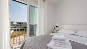 A hotel room with a bed, a nightstand, a window with curtains, and a view of buildings outside.