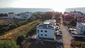 A coastal residential area with modern buildings, a parking lot, and a view of the sea.