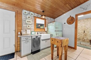 Une cuisine avec un plafond en bois, un réfrigérateur turquoise d’époque, un évier et un tabouret en bois.