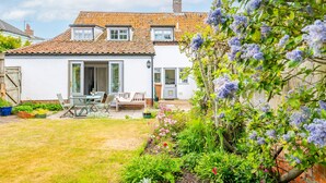 A house with a tiled roof, a garden with various plants, and a patio area with outdoor furniture.