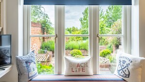 A window seat with a view of a garden, a white cushion with "Beach Life" text, and a striped pillow.