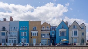 A row of colorful seaside buildings with bay windows and balconies, a clear sky, and a pebble beach in the foreground.