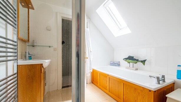 A modern bathroom with a skylight, a wooden vanity, a white sink, and a fish decoration.
