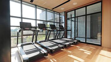 Un gimnasio con cintas de correr alineadas, ventanas amplias y suelo de madera.