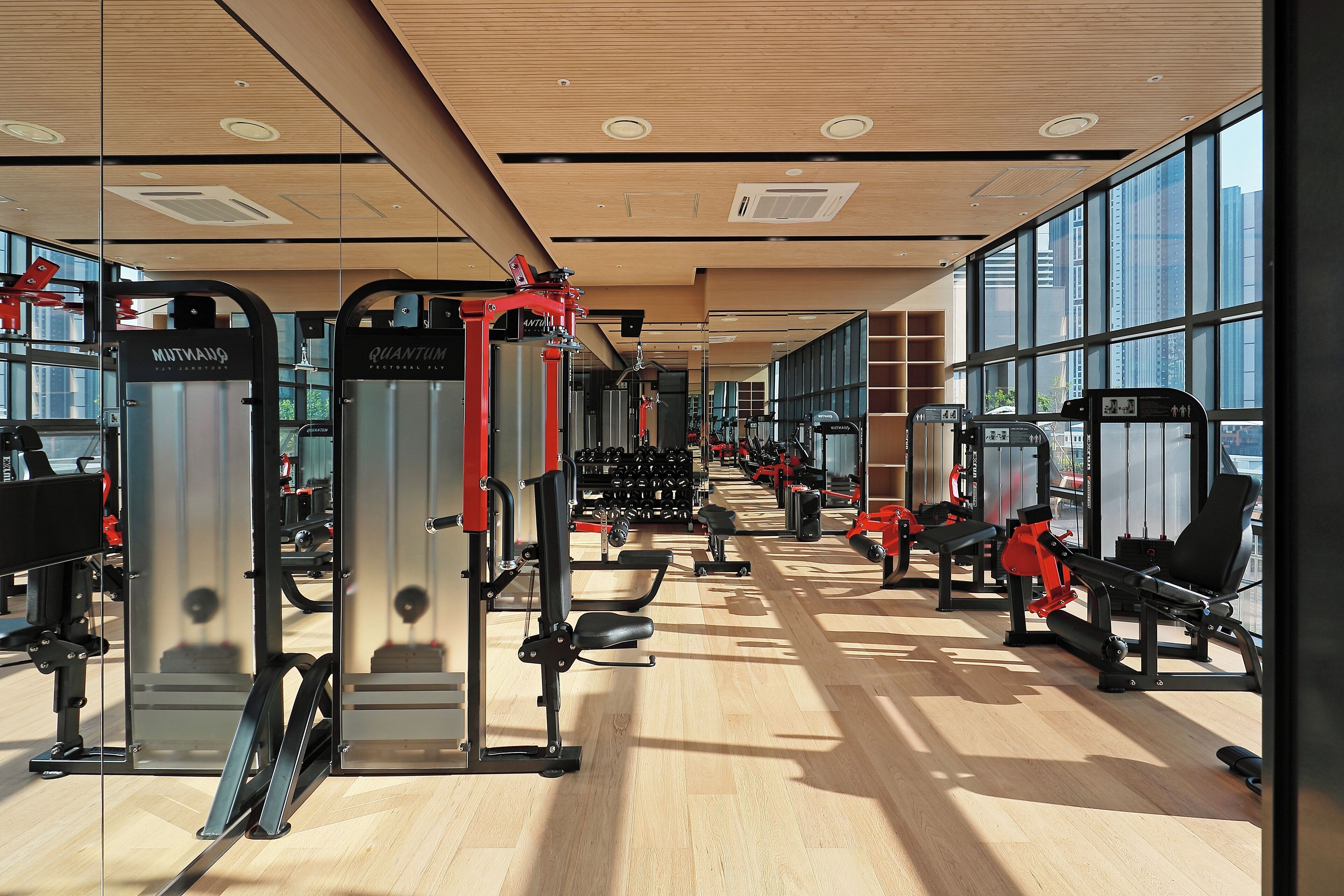 Een moderne sportschool met diverse fitnessapparaten, grote ramen en een houten vloer.