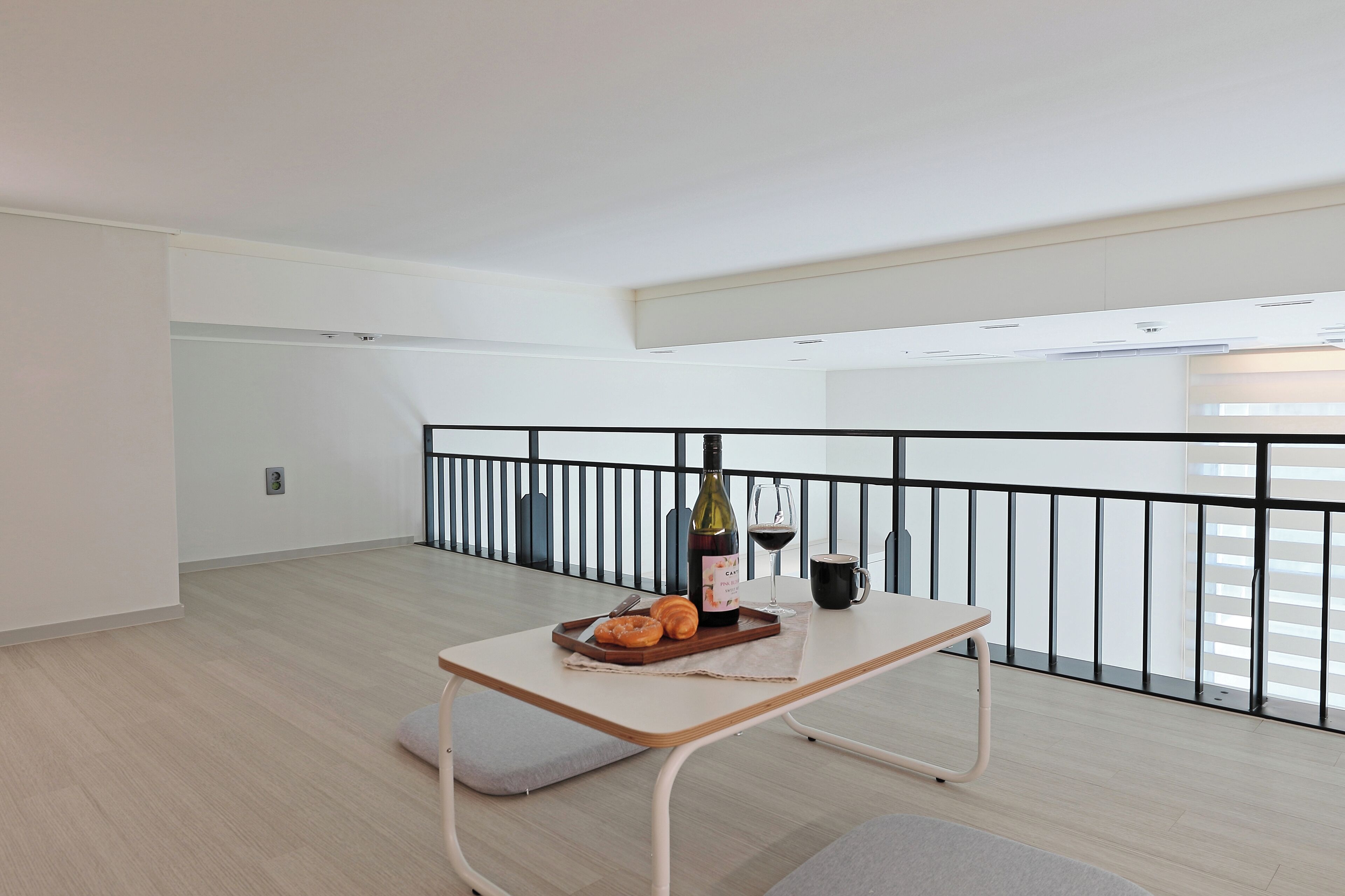 A minimalist dining area with a table set for two, featuring a bottle of wine, a glass, and a tray with pastries.