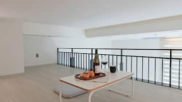 A minimalist dining area with a table set for two, featuring a bottle of wine, a glass, and a tray with pastries.