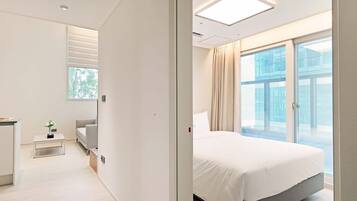 A modern hotel room with a bed, a small desk, a sofa, and a large window with a view of the city.