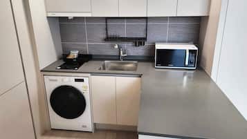 Cocina compacta con lavadora, microondas y lavamanos pequeño.