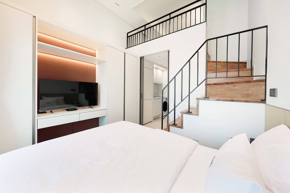 Une chambre moderne avec un grand lit, une télévision et un escalier.