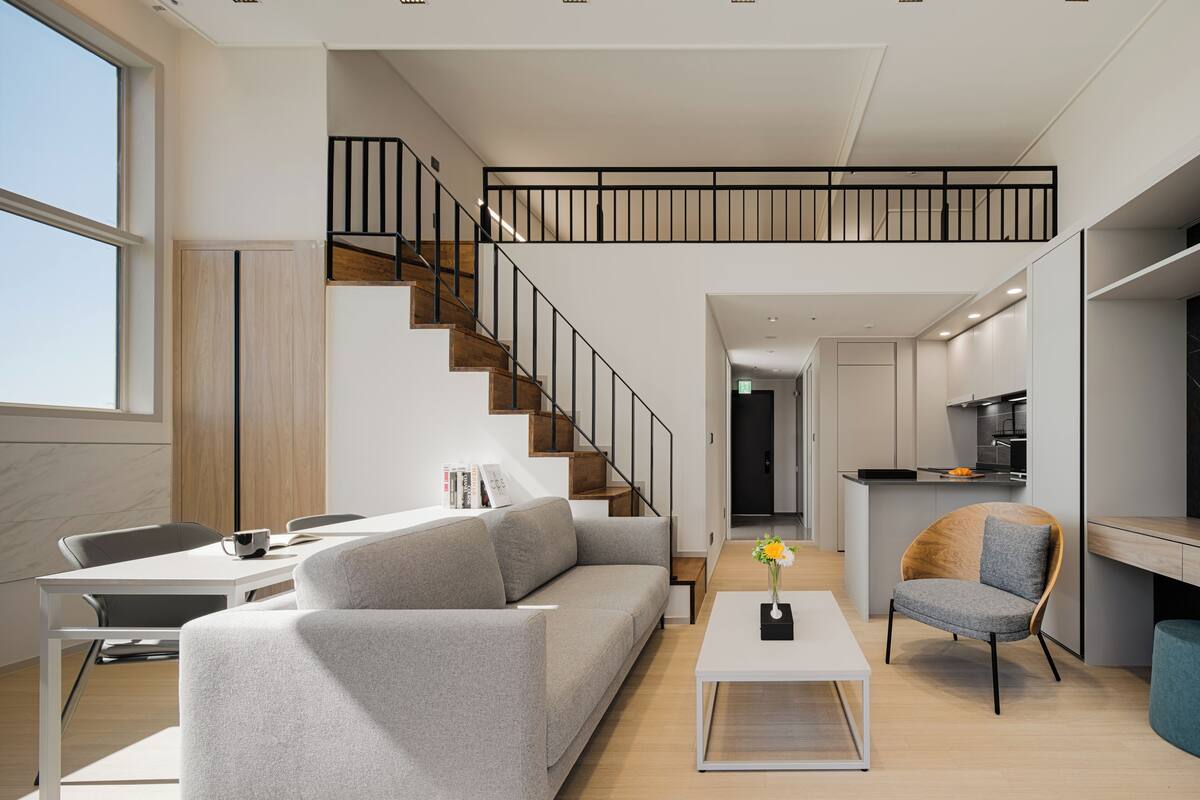 Un salon moderne avec un canapé gris, une table basse et un escalier avec des marches en bois et des rampes noires.